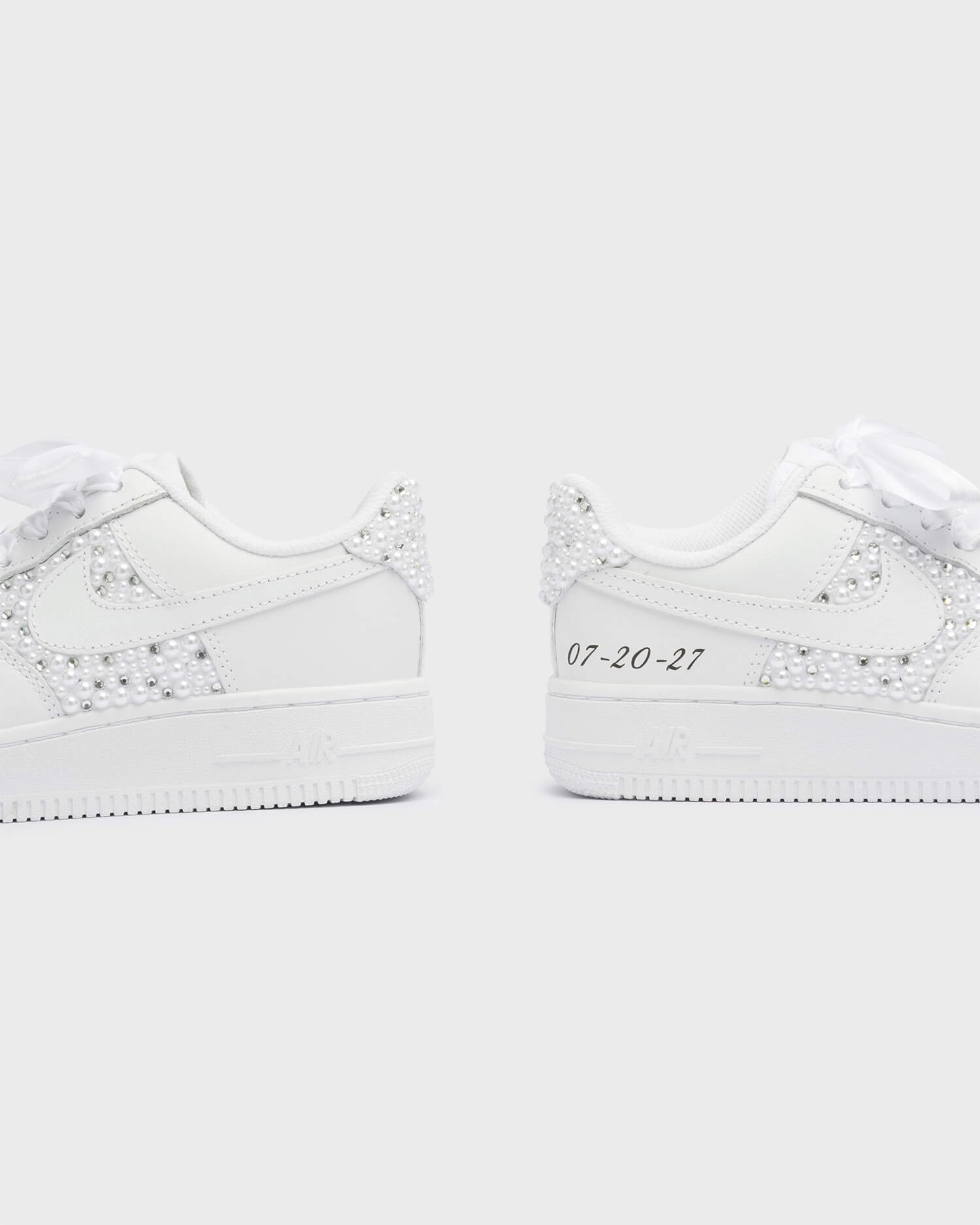 Custom white Air Force 1 wedding sneakers with pearl decorations and a personalized date on the heel. Elegant bridal sneakers with satin laces and handcrafted embellishments, perfect for a unique wedding look.