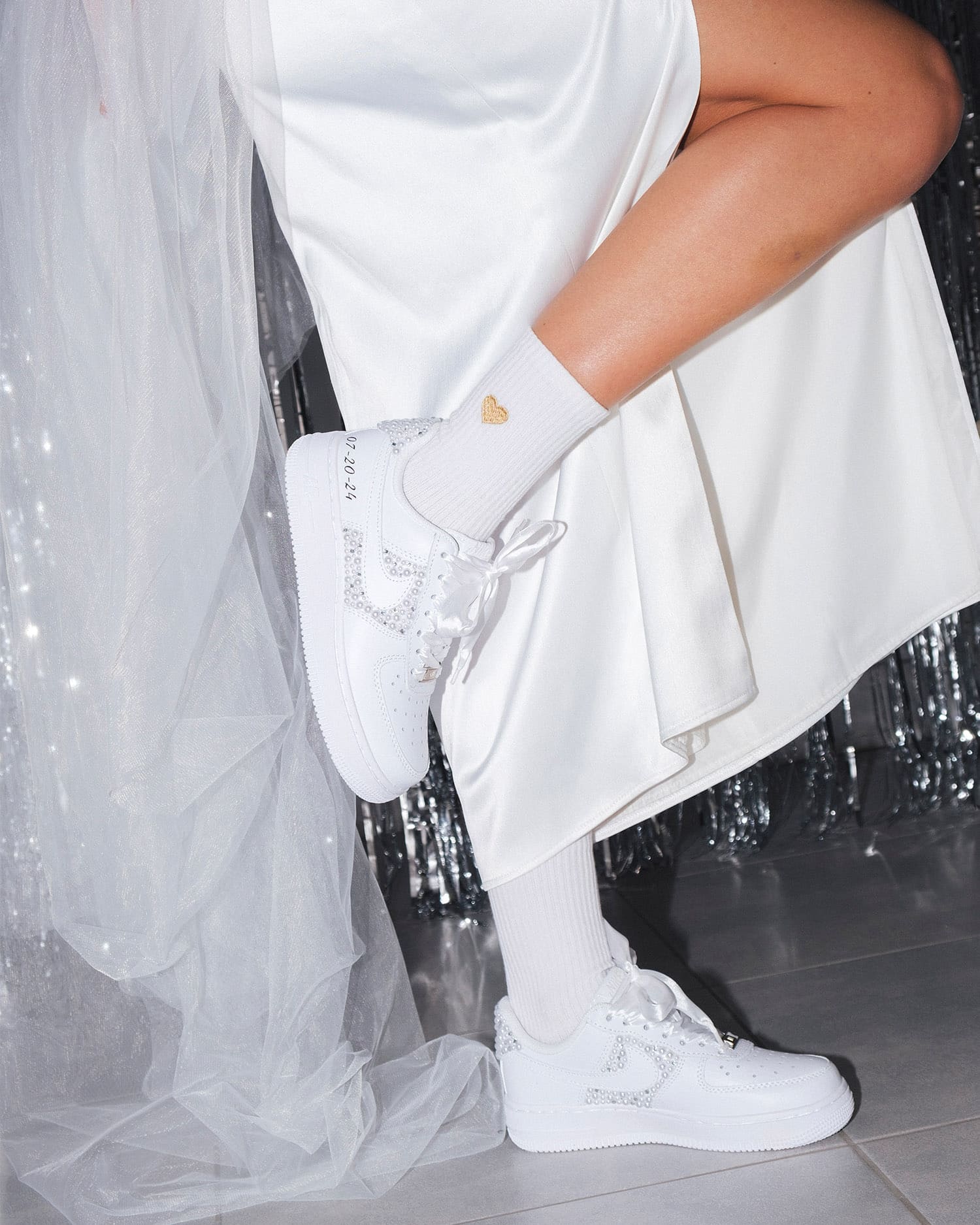 Bride wearing custom white Air Force 1 wedding sneakers with pearl details. A stylish and comfortable bridal look with satin laces and a personalized date on the side.
