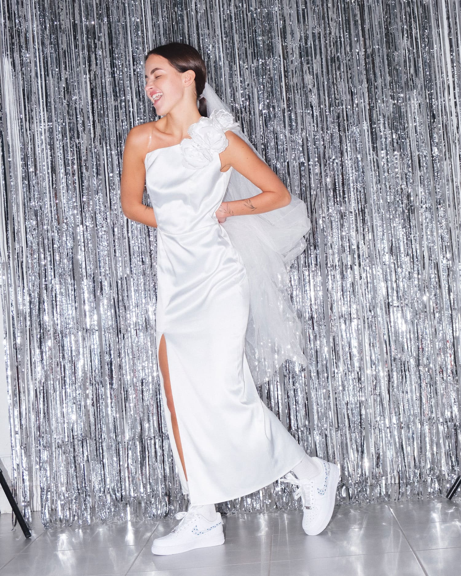 Happy bride in a wedding dress wearing custom Air Force 1 sneakers with pearl details. A modern twist on bridal footwear for a stylish wedding.