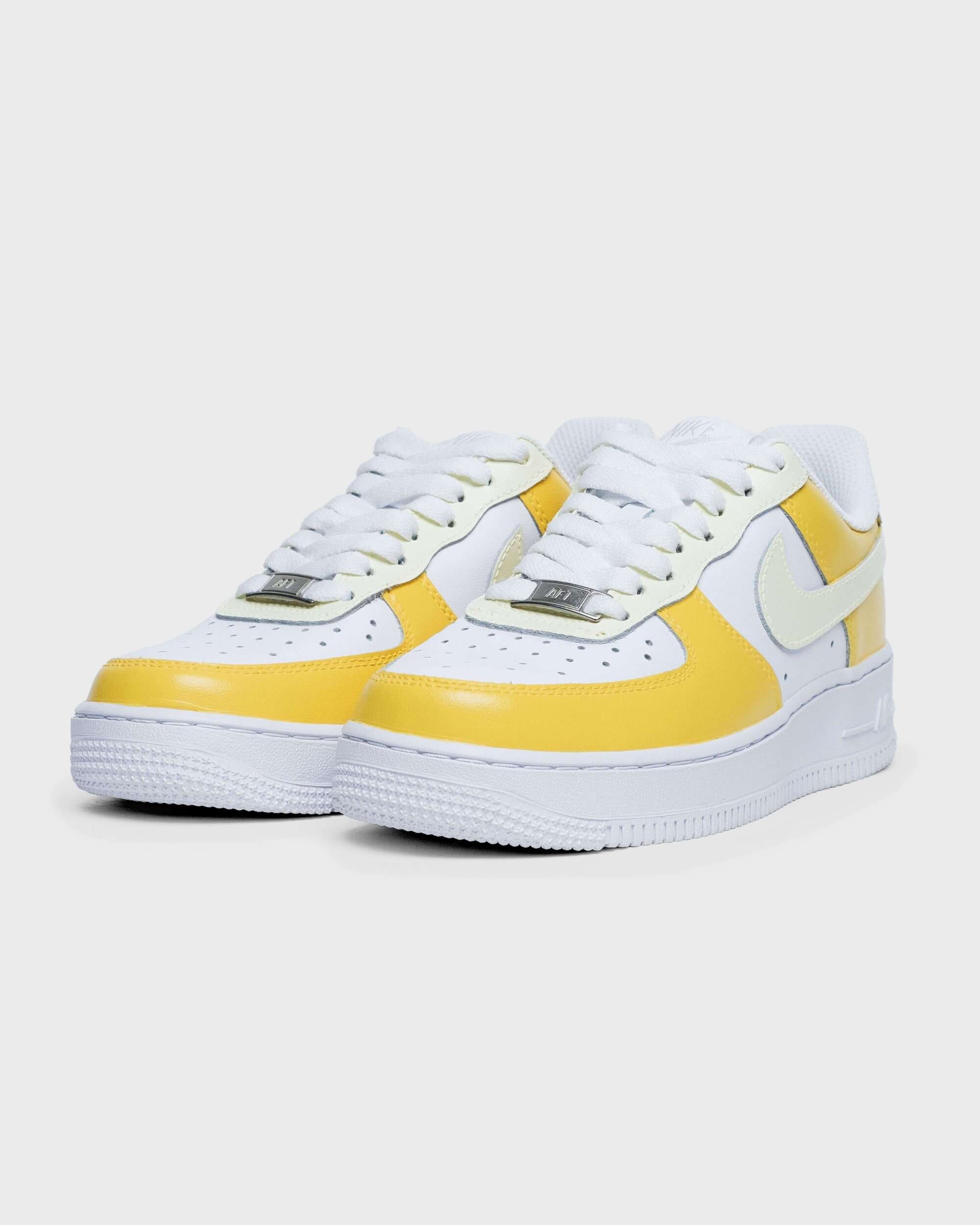 Angled view of sneaker pair: Yellow and white custom Air Force 1 sneakers, angled view showing the side and front details of the shoes.