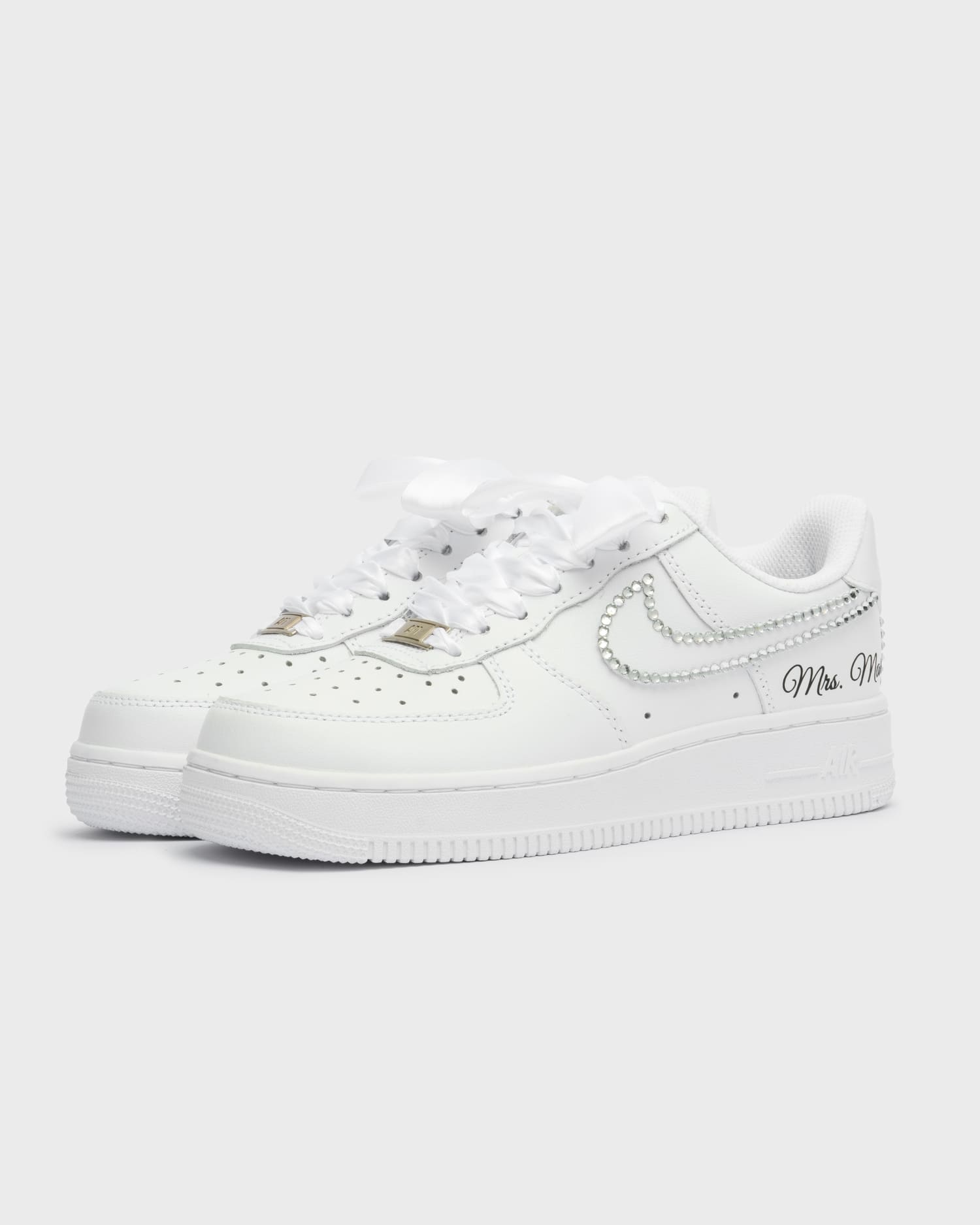 Custom white Air Force 1 wedding sneakers with rhinestone swoosh. Handcrafted bridal shoes with satin laces and personalized 'Mrs. Mary' embroidery. Elegant and stylish wedding footwear.