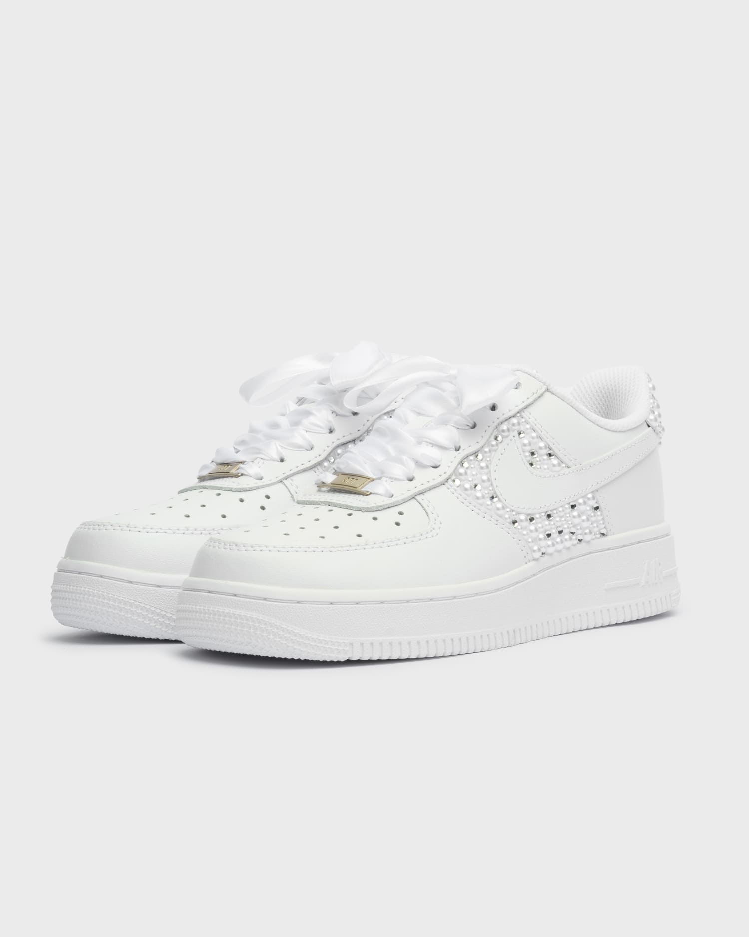 Custom white Air Force 1 sneakers with pearl details on the swoosh and heel. Luxury handcrafted bridal shoes with satin laces, ideal for a wedding or special occasion. Personalized wedding sneakers with elegant embellishments.