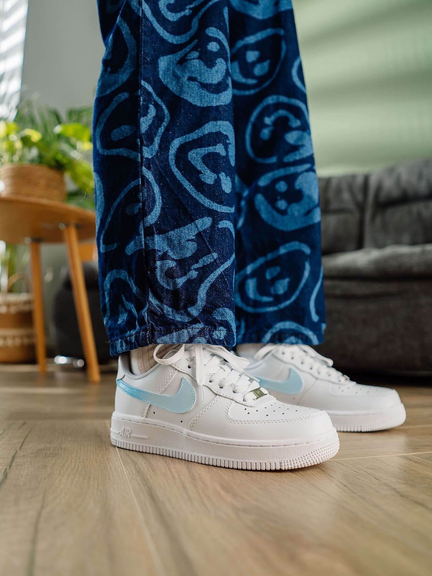 Close-up of model wearing custom white Air Force 1 sneakers with a light blue swoosh, styled with patterned blue jeans, highlighting the sneakers’ unique and personalized design.