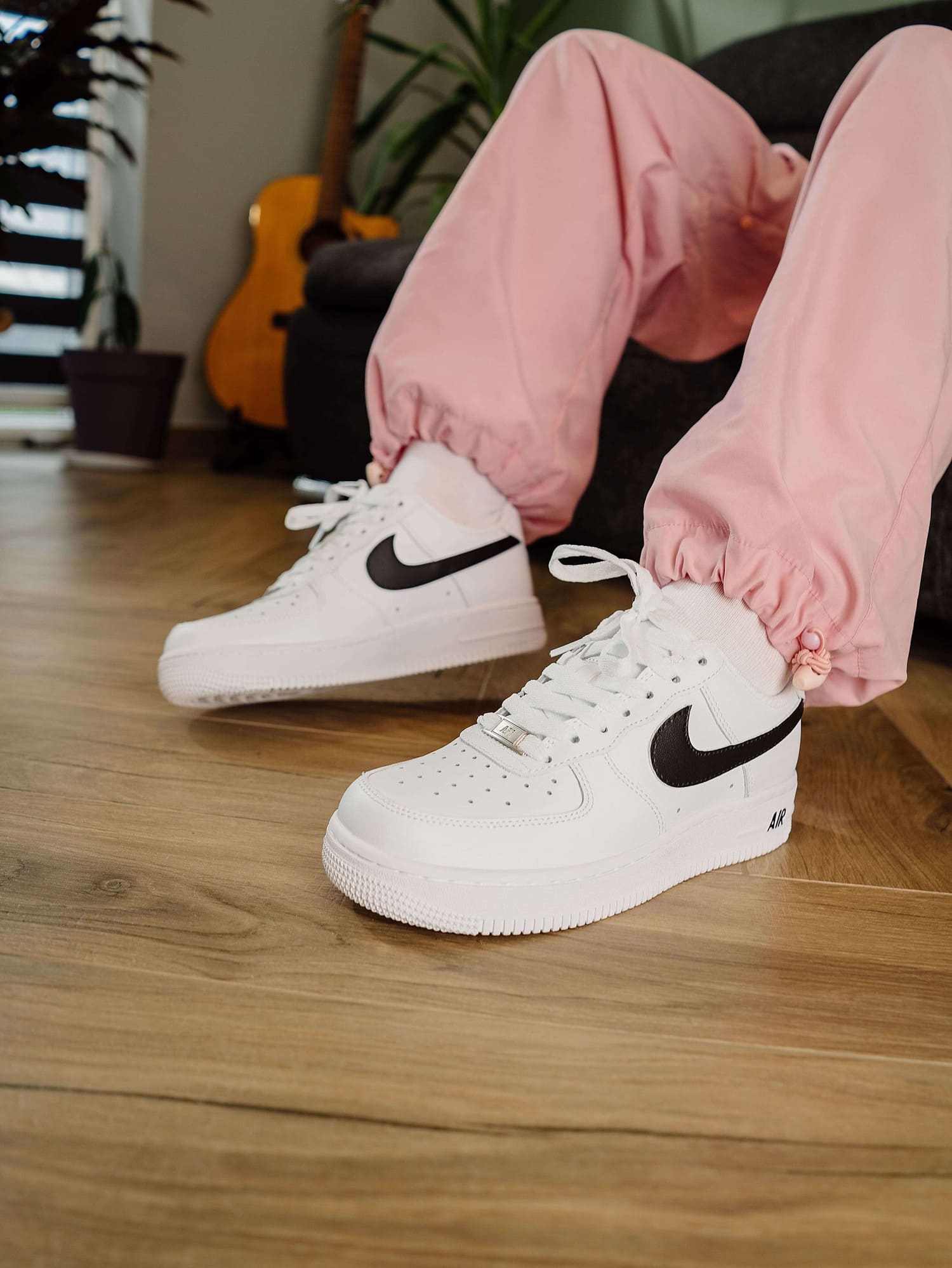 Customized Nike Air Force 1 shoes with black swoosh, close-up of feet in pink pants, emphasizing the shoe's sleek and stylish appearance.