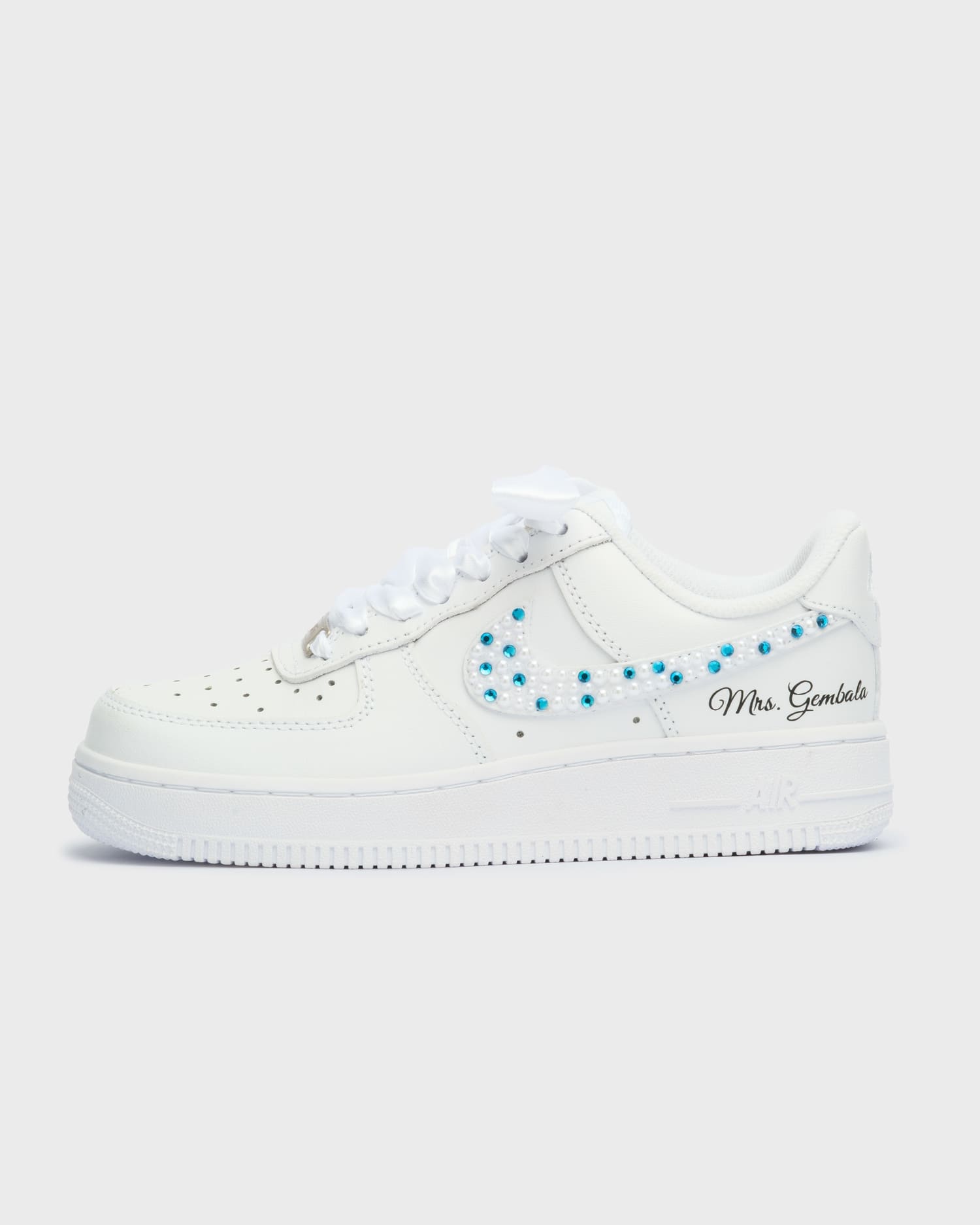 White Air Force 1 custom wedding sneakers with blue and white pearl embellishments on the swoosh. Personalized bridal shoes featuring 'Mrs. Gembala' embroidery. A stylish and unique choice for brides.