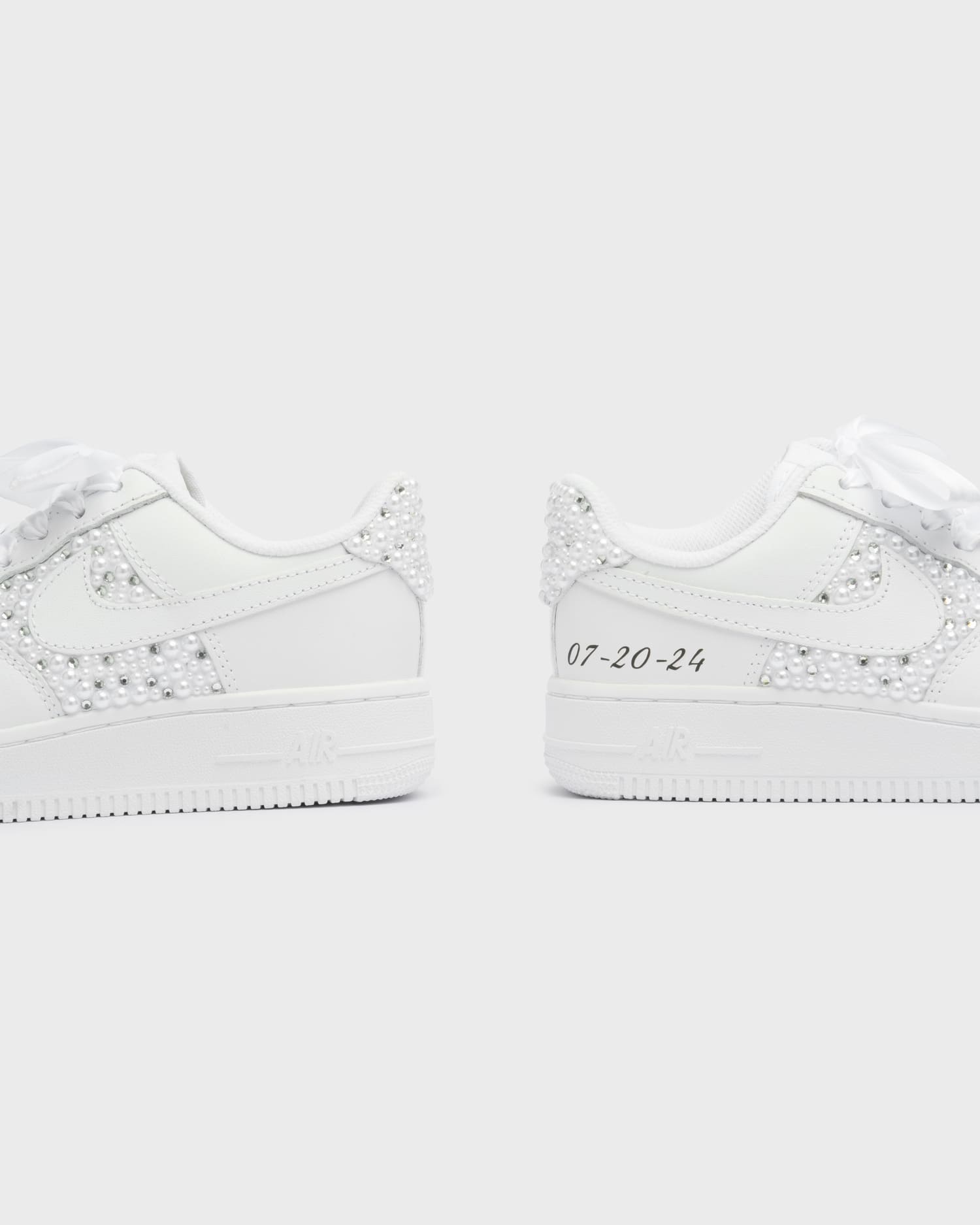 Custom white Air Force 1 wedding sneakers with pearl decorations and a personalized date on the heel. Elegant bridal sneakers with satin laces and handcrafted embellishments, perfect for a unique wedding look.