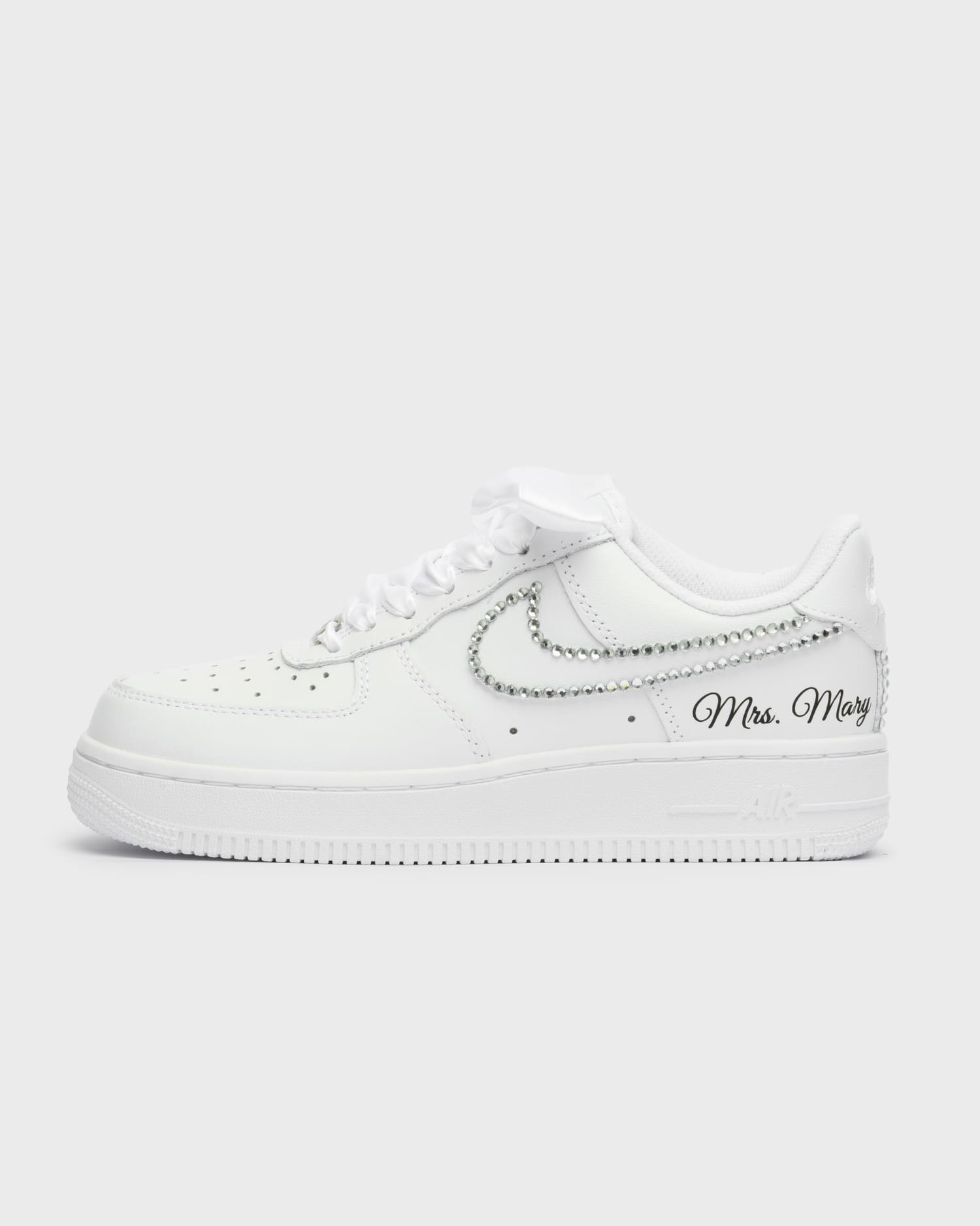White Air Force 1 custom bridal sneakers with shimmering rhinestones on the swoosh. Personalized wedding shoes with 'Mrs. Mary' embroidery and satin laces, perfect for brides seeking a luxurious touch.