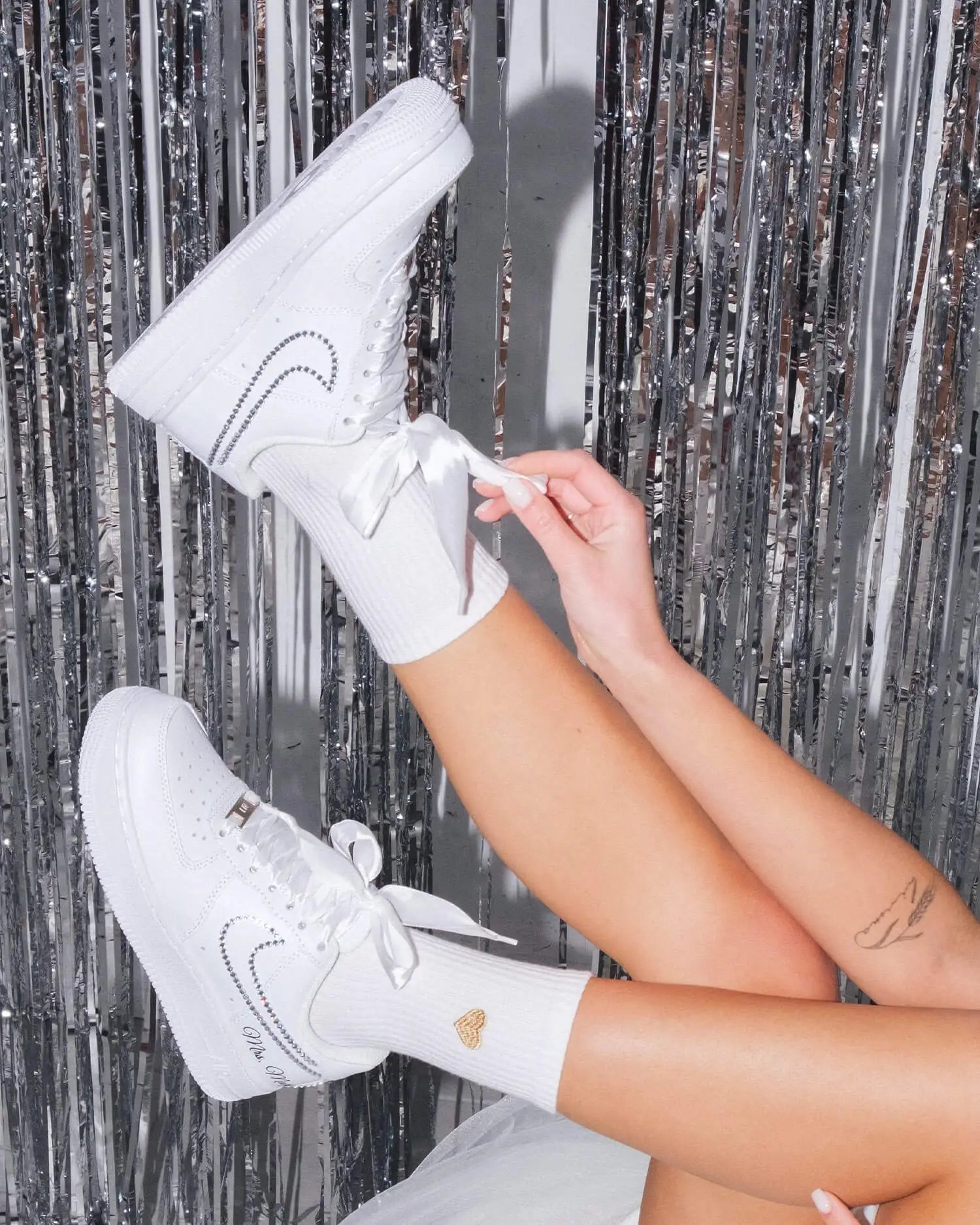 White sneakers with a heart design worn by a person against a metallic tinsel background