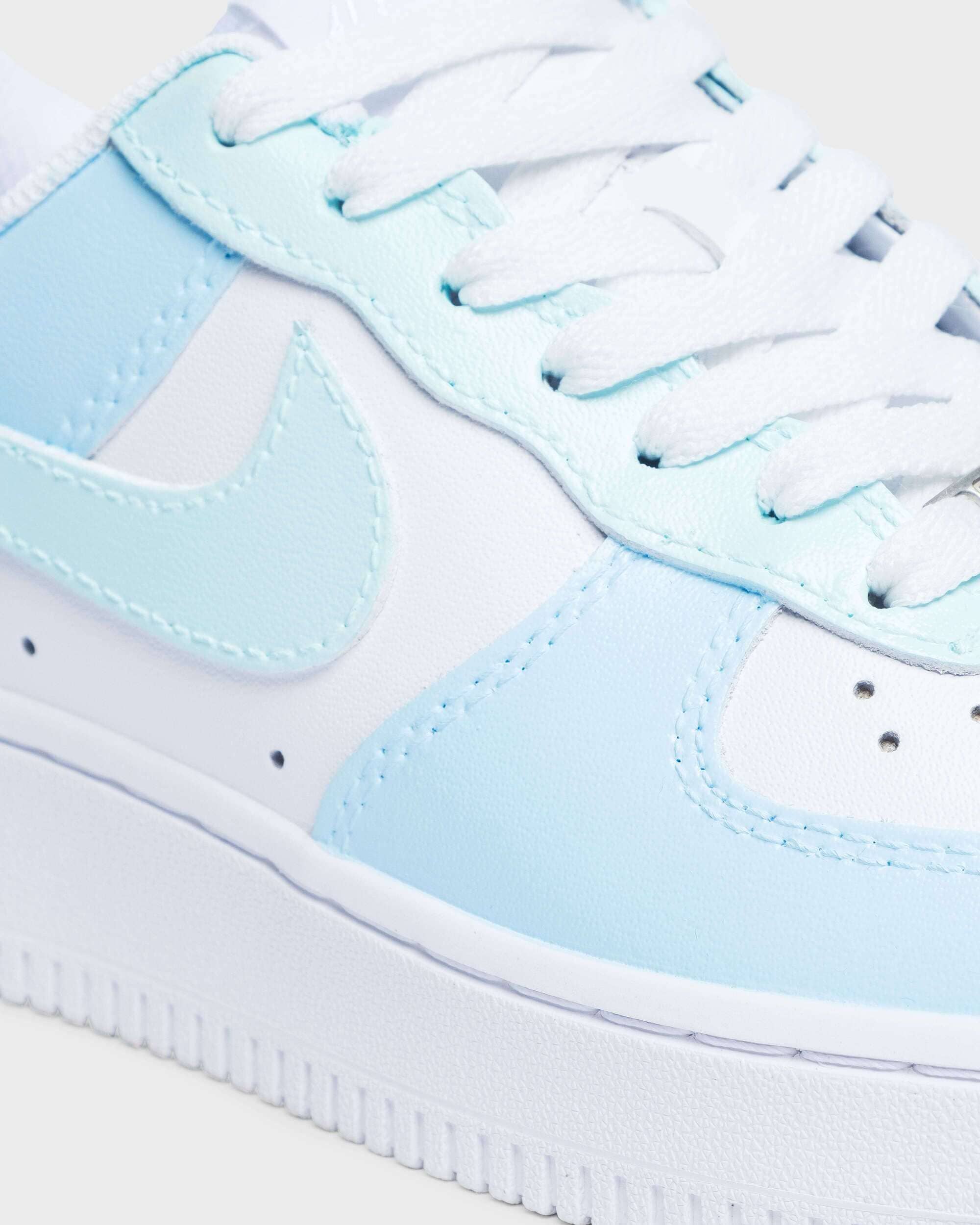 Close-up of custom Air Force 1 sneaker with light blue overlays and swoosh on a white leather base, emphasizing the clean stitching and soft color palette for a unique look.