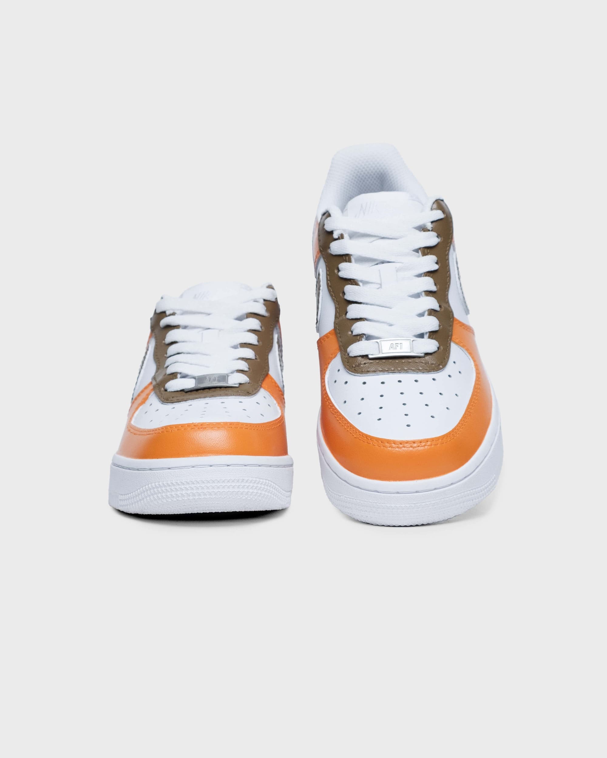 Front view of custom Air Force 1 sneakers featuring bright orange and brown accents, with a perforated toe box and white laces for a standout, contemporary look.