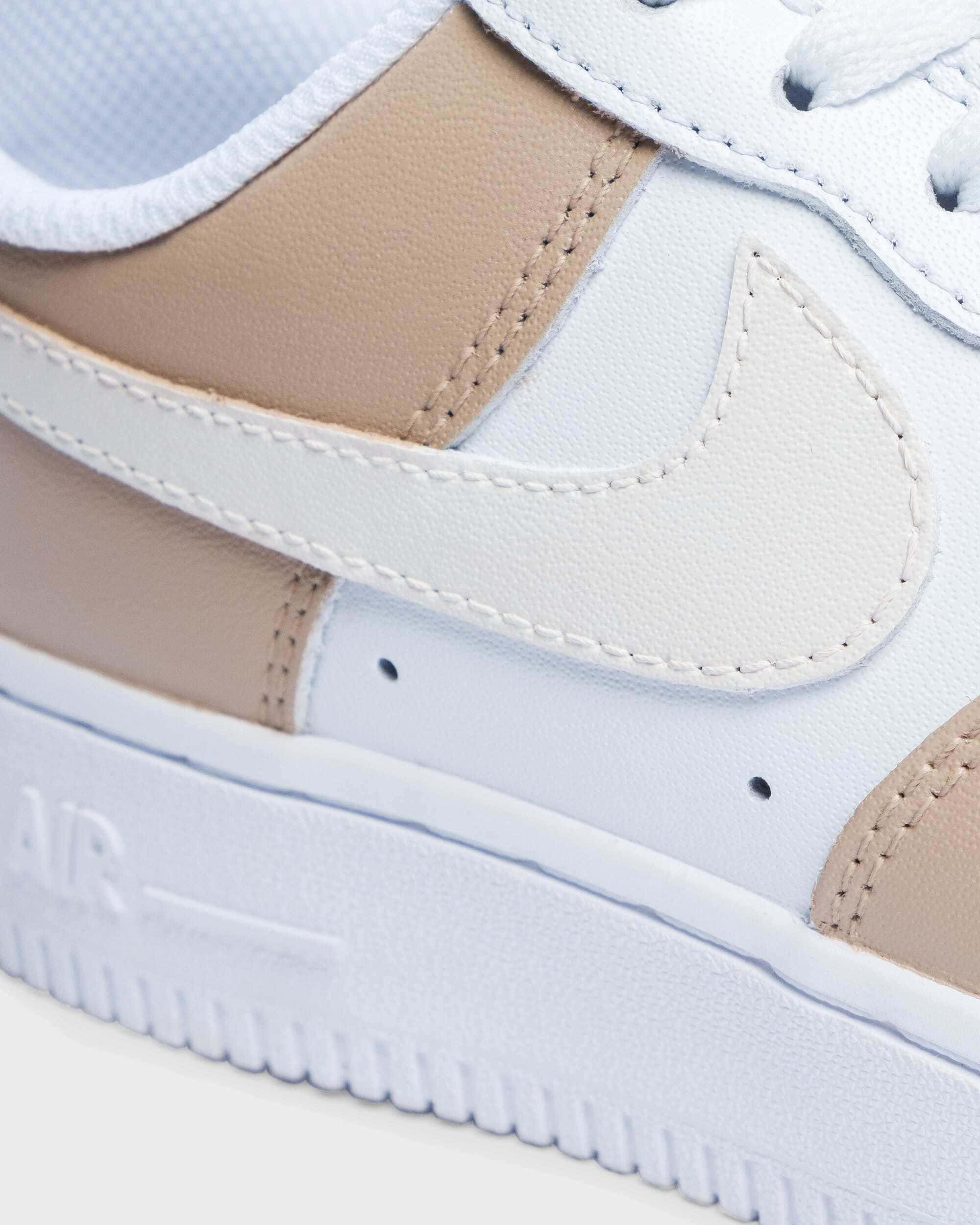 Close-up detail of hand-painted custom Air Force 1 sneaker in cream tones, highlighting the stitching and design on the Swoosh logo.