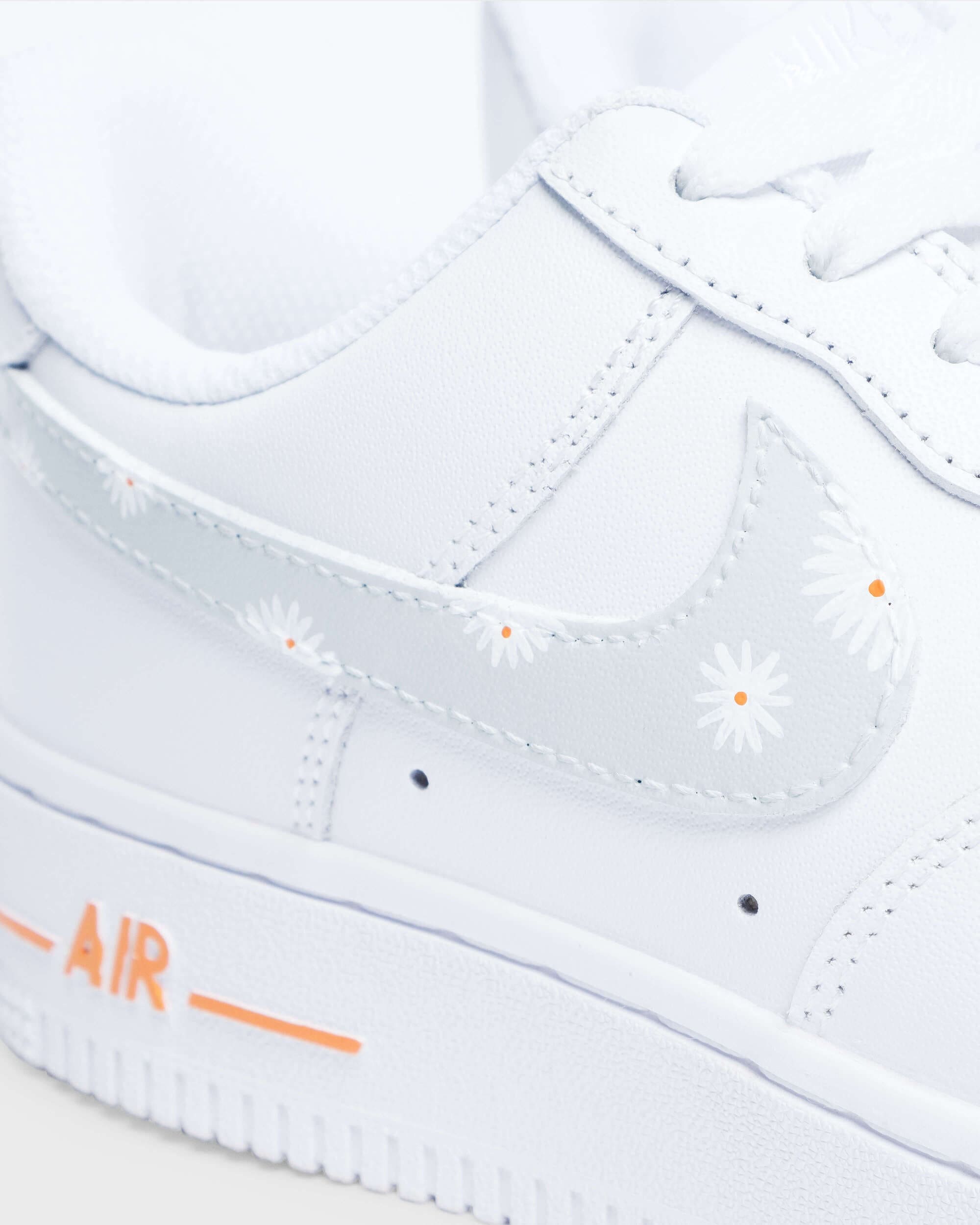 Close-up of custom Air Force 1 sneaker with hand-painted white flower details on a light gray Swoosh.