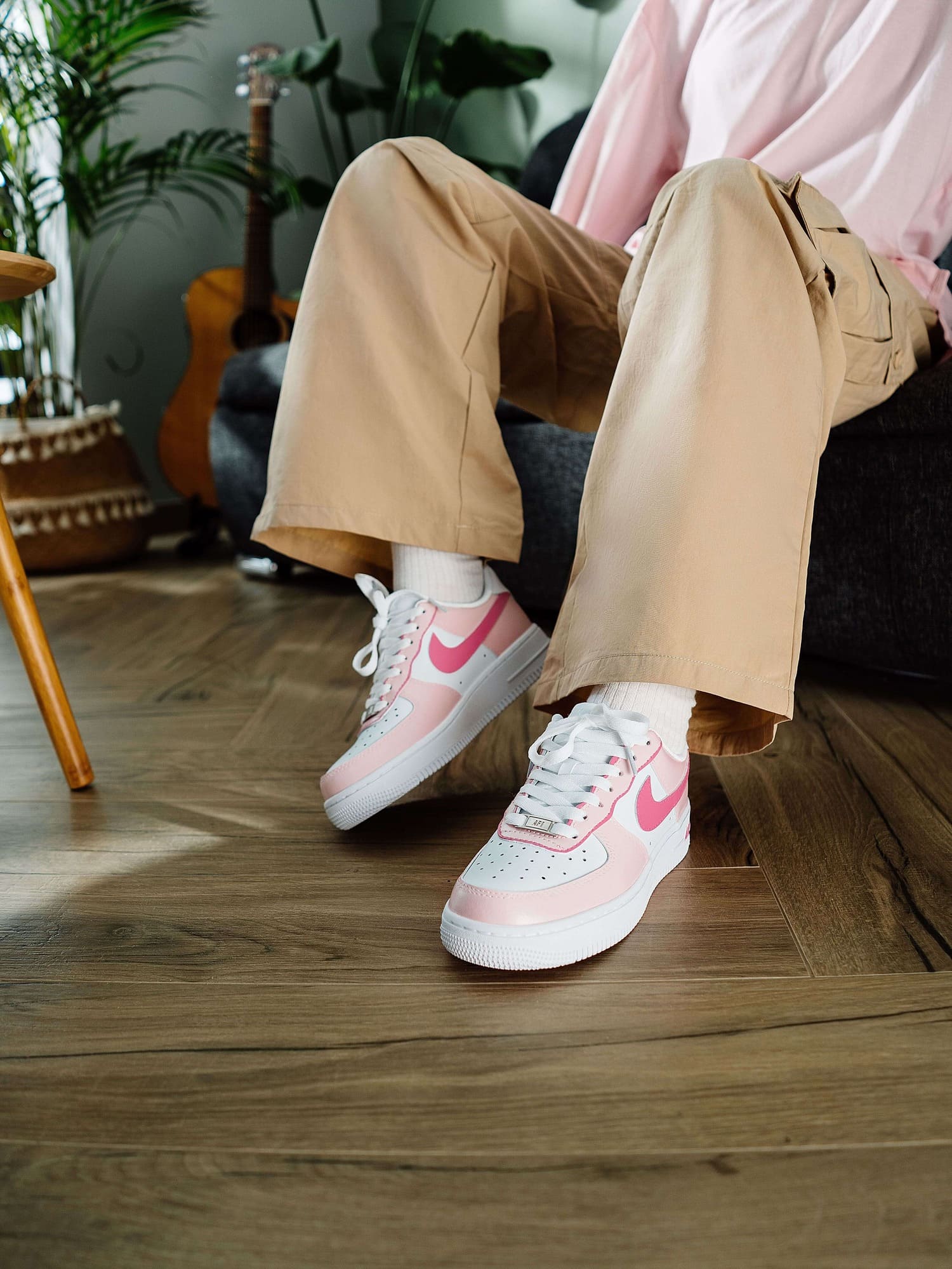 Model's legs crossed while wearing custom pink Air Force 1 sneakers, styled with beige pants and a relaxed fit, highlighting the comfortable and unique sneaker design.