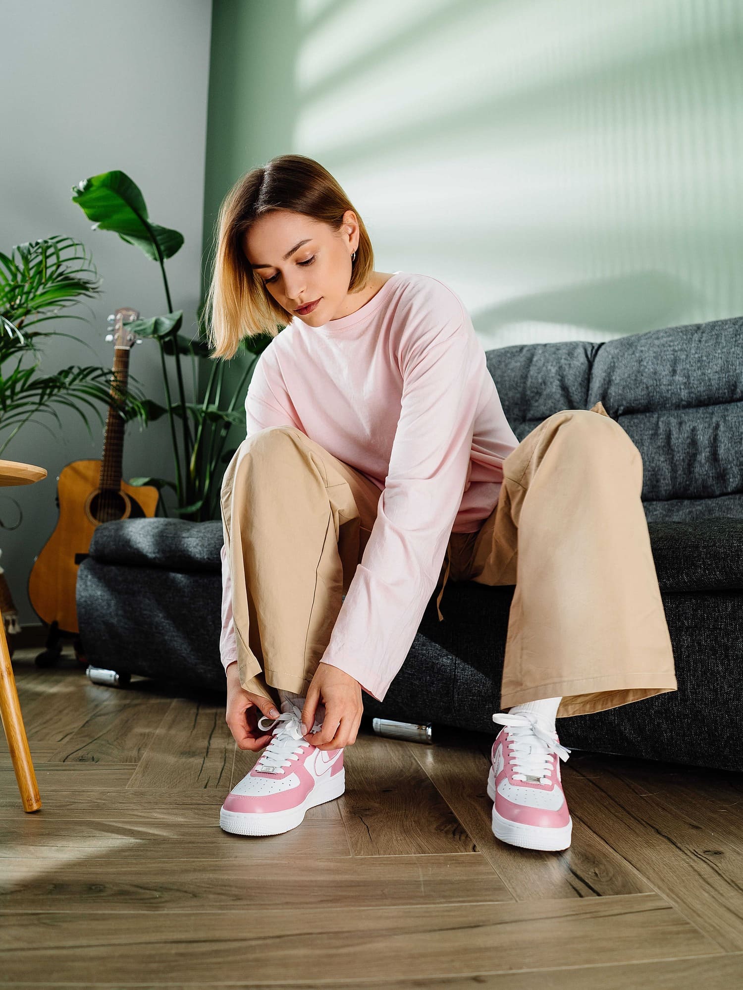 Woman lacing up pink custom Air Force 1 sneakers while seated indoors – a lifestyle shot featuring the stylish custom pink and white Nike sneakers.