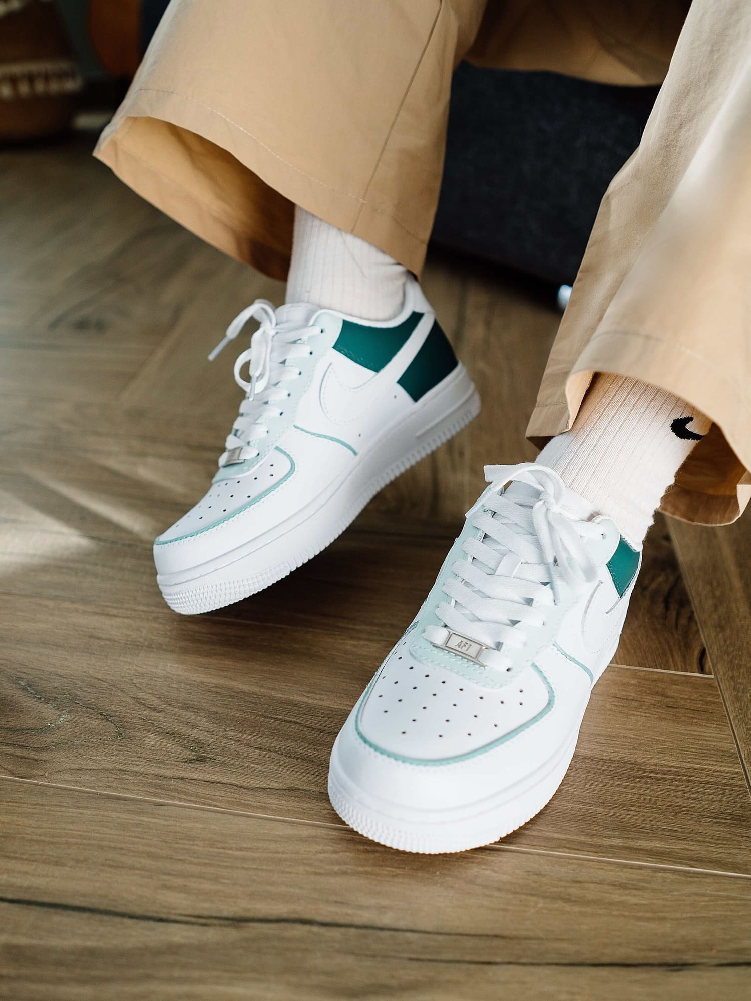 Custom Air Force 1 sneakers in white and teal green, styled with beige pants for a trendy look.