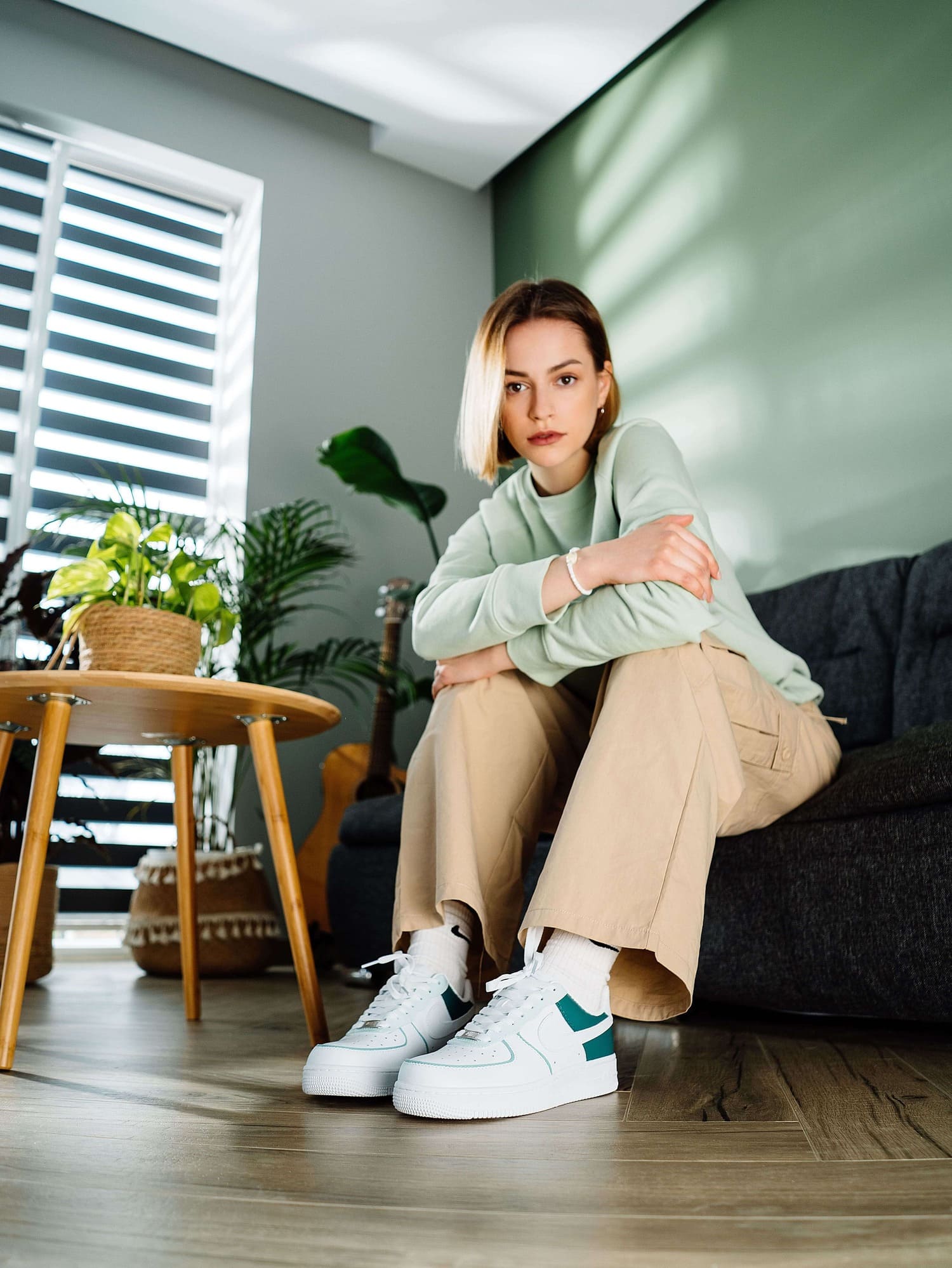 Model wearing custom teal green and white Air Force 1 sneakers, paired with casual beige pants.