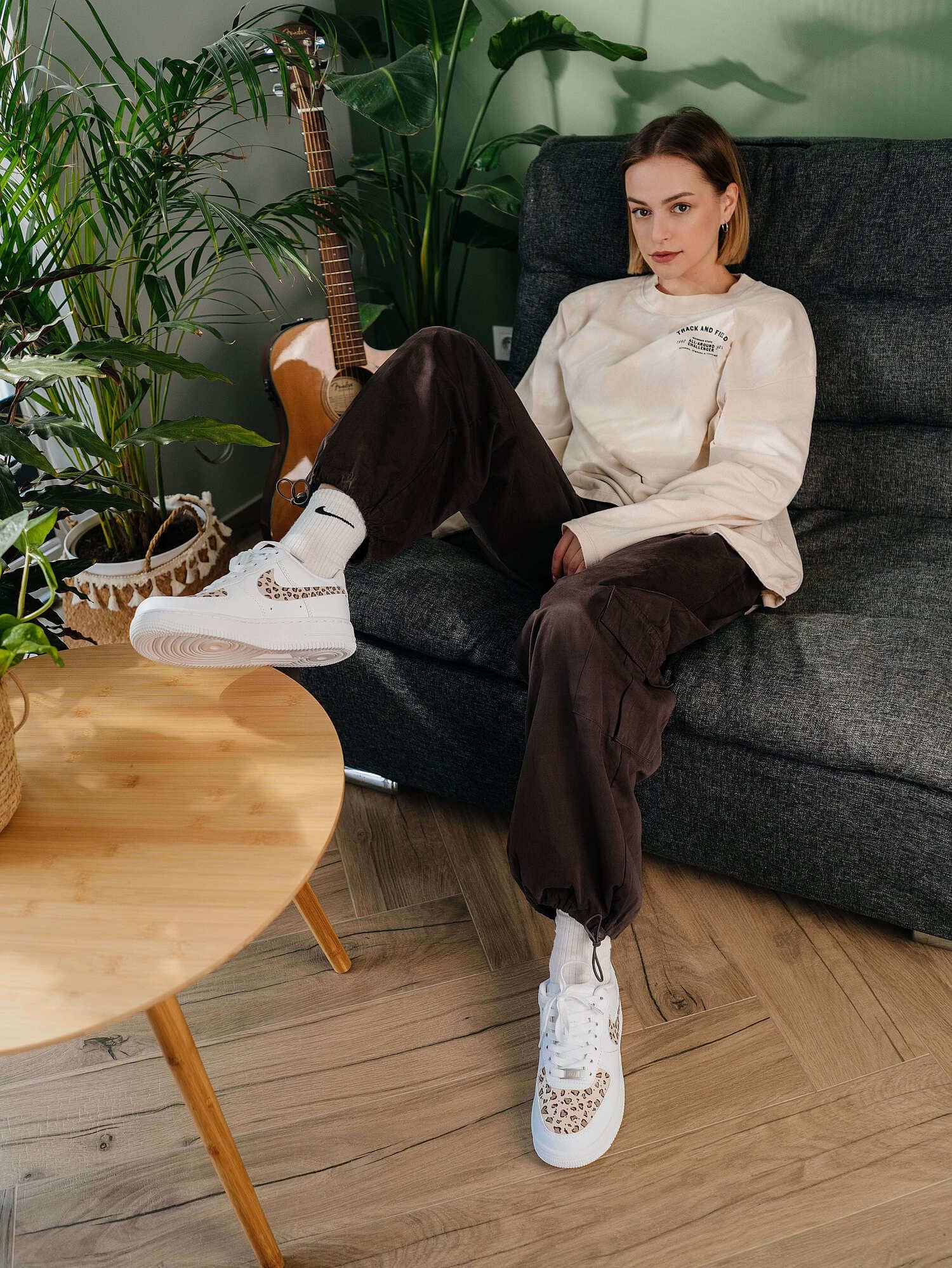 Model sitting on a couch, wearing custom Air Force 1 sneakers with leopard print, styled with a casual outfit, highlighting the bold animal print for a fashionable look.