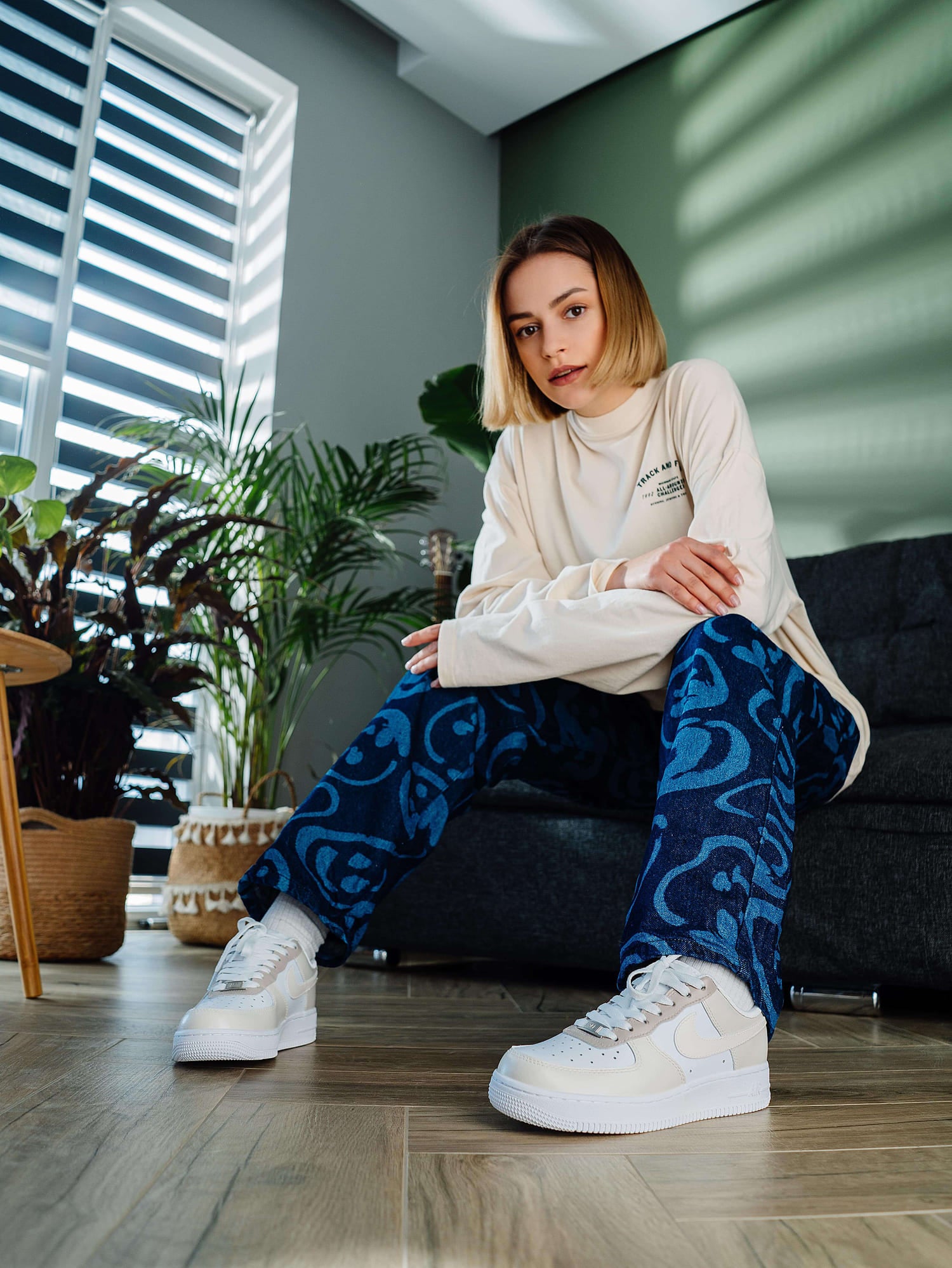 Model sitting while wearing custom beige and white Air Force 1 sneakers, highlighting the hand-painted, minimalist design for a soft, modern aesthetic.