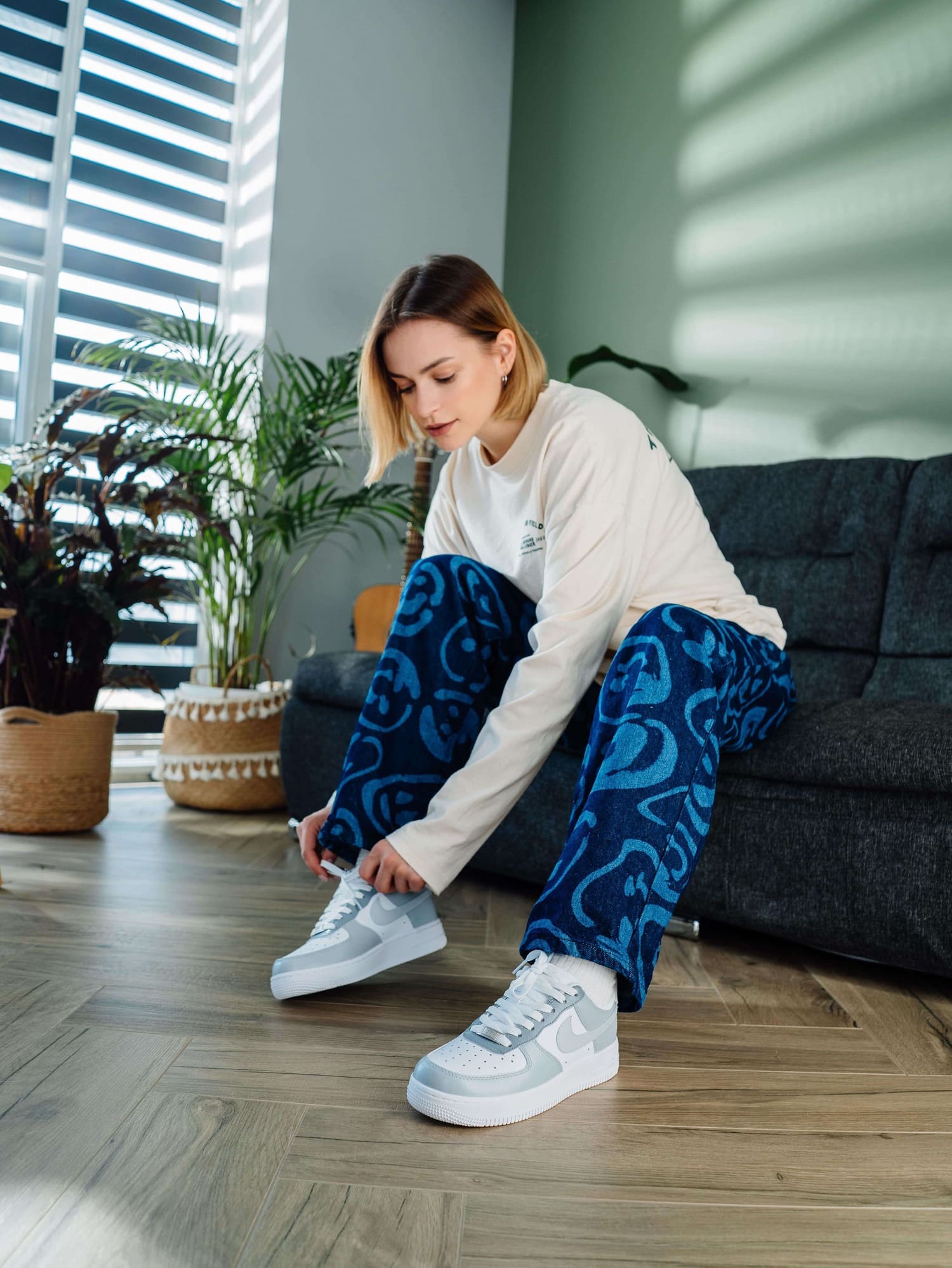 Model adjusting custom Air Force 1 sneakers with light gray swoosh, styled with patterned blue jeans, creating a relaxed, fashionable look.