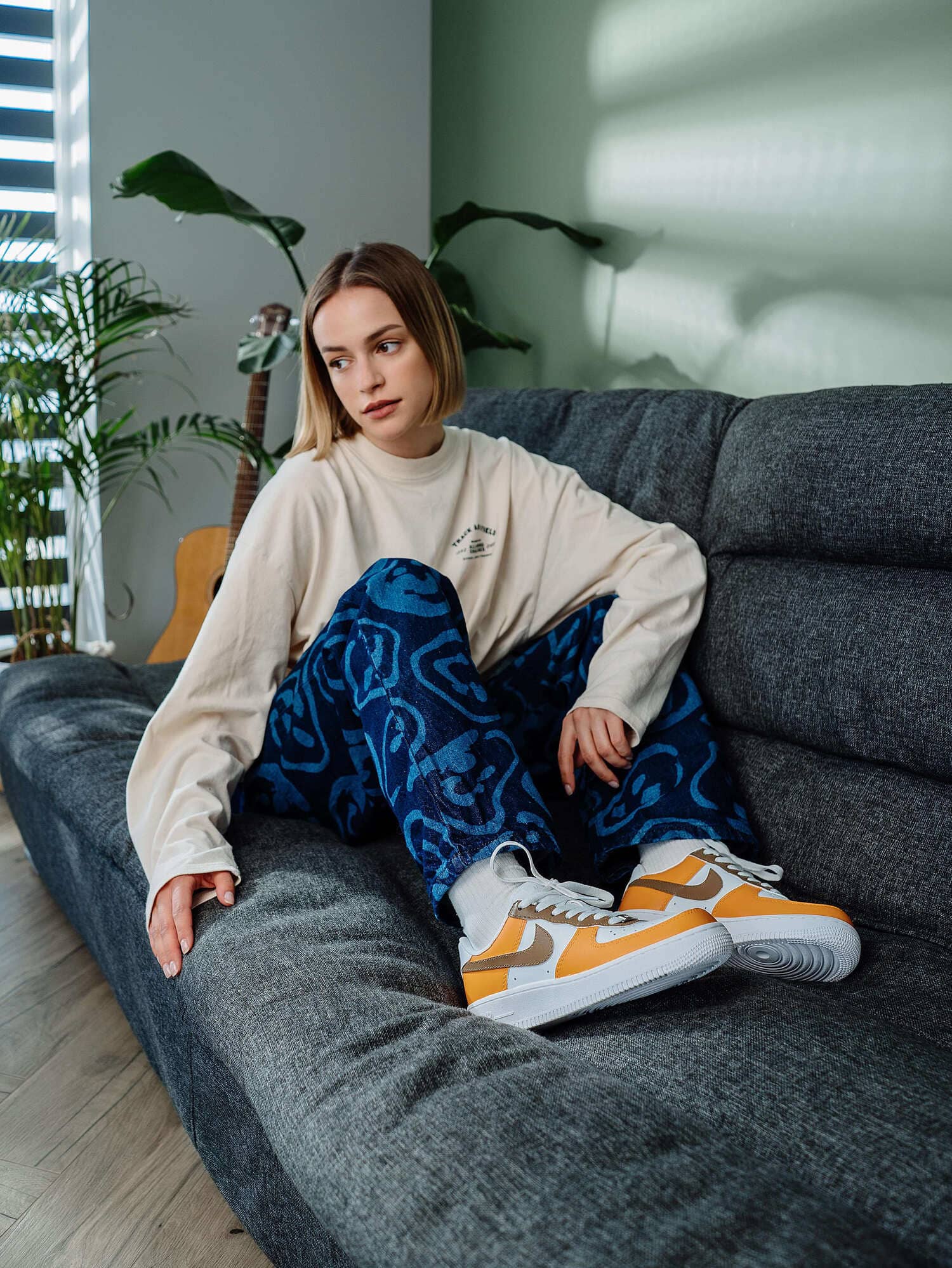 Model sitting on a couch, wearing custom orange and brown Air Force 1 sneakers with a relaxed outfit, highlighting a stylish, personalized look.