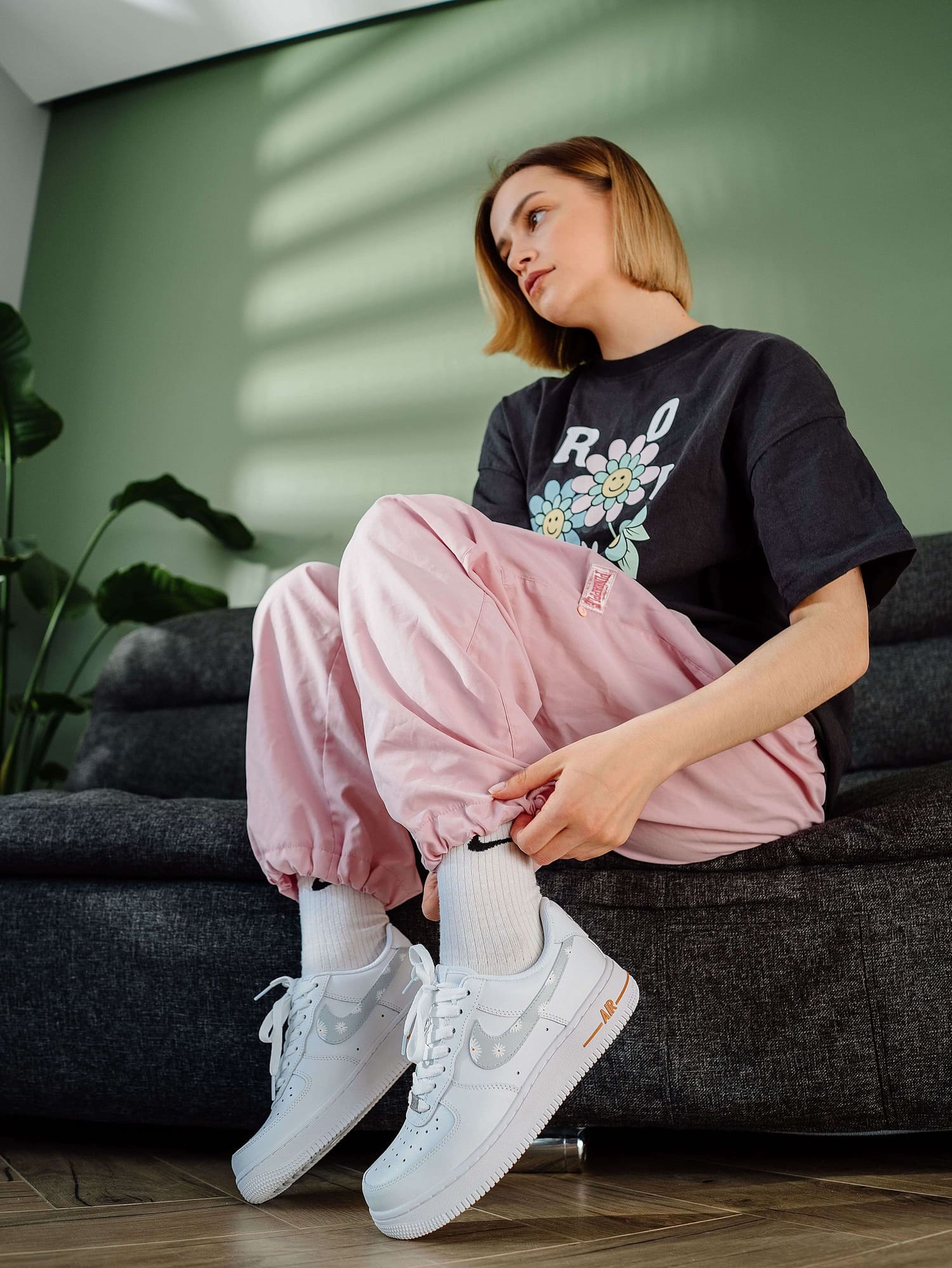 Model wearing custom Air Force 1 sneakers with hand-painted flowers, sitting in a stylish room.