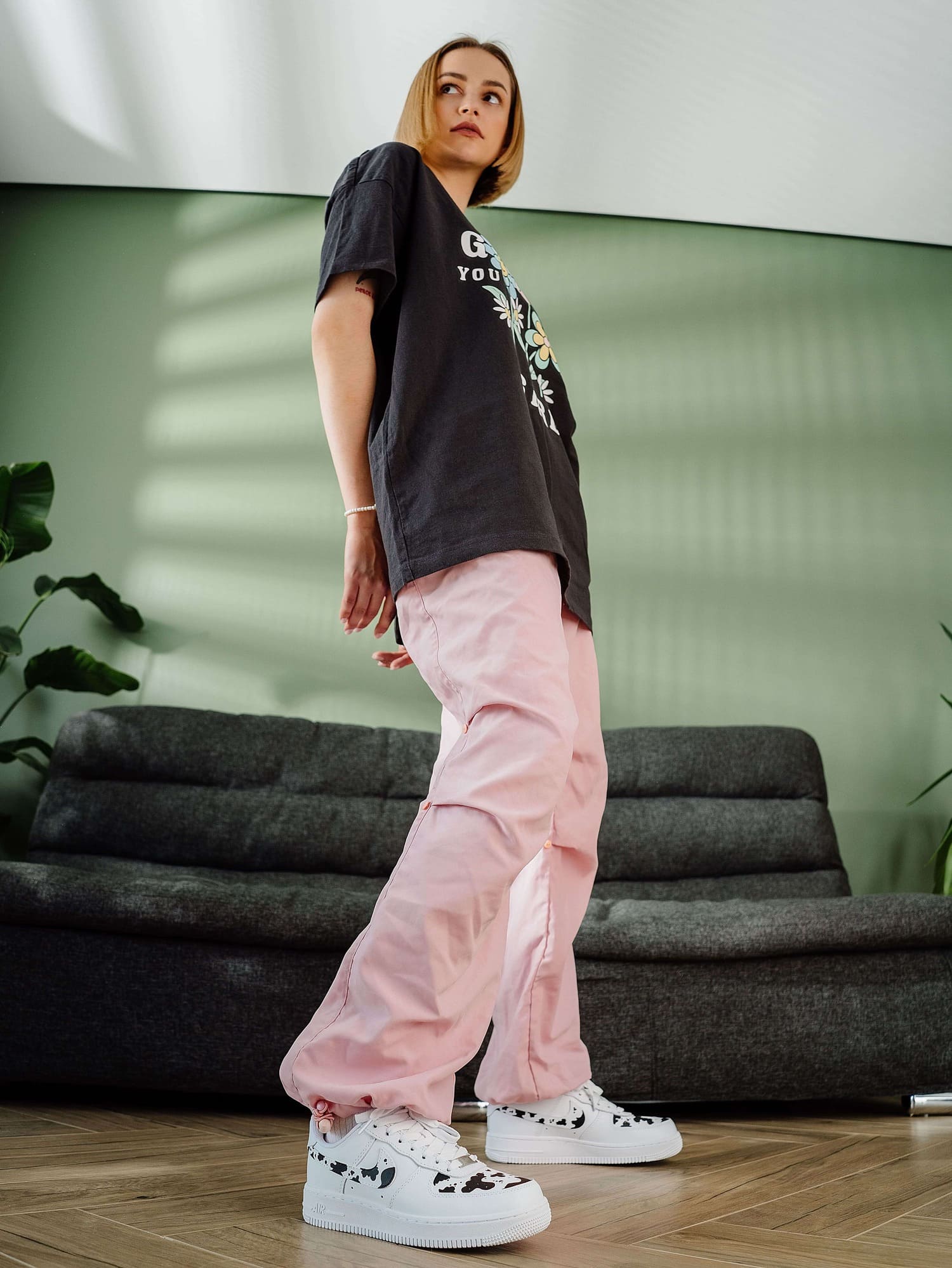 Model wearing custom Air Force 1 sneakers with cow print design, posing in a modern room.