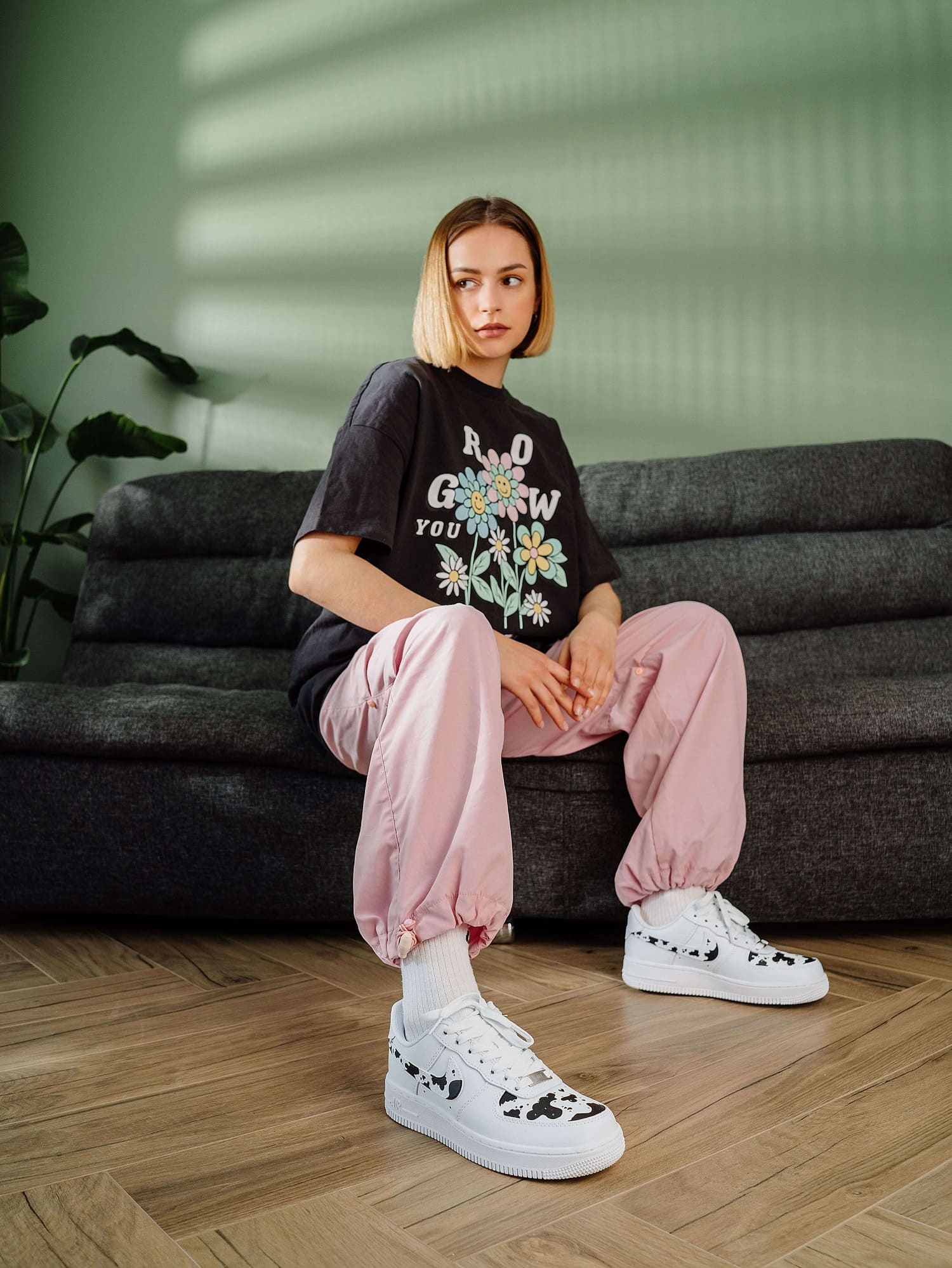 Model sitting and wearing custom Air Force 1 sneakers with hand-painted cow print, adding a playful design element.