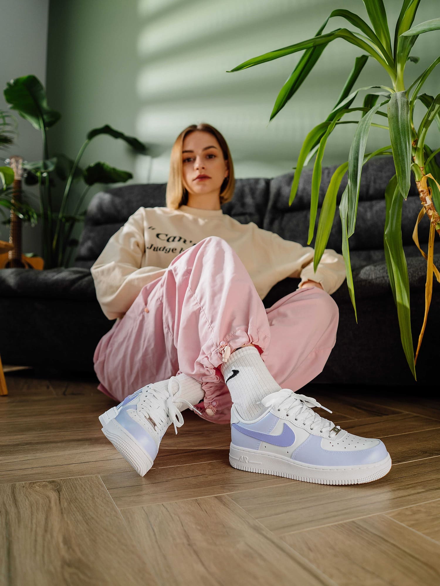 Model wearing custom Nike Air Force 1 in pastel purple, sitting casually on the floor - Fashionable hand-painted Air Force 1 in lavender, designed for a casual yet stylish look.