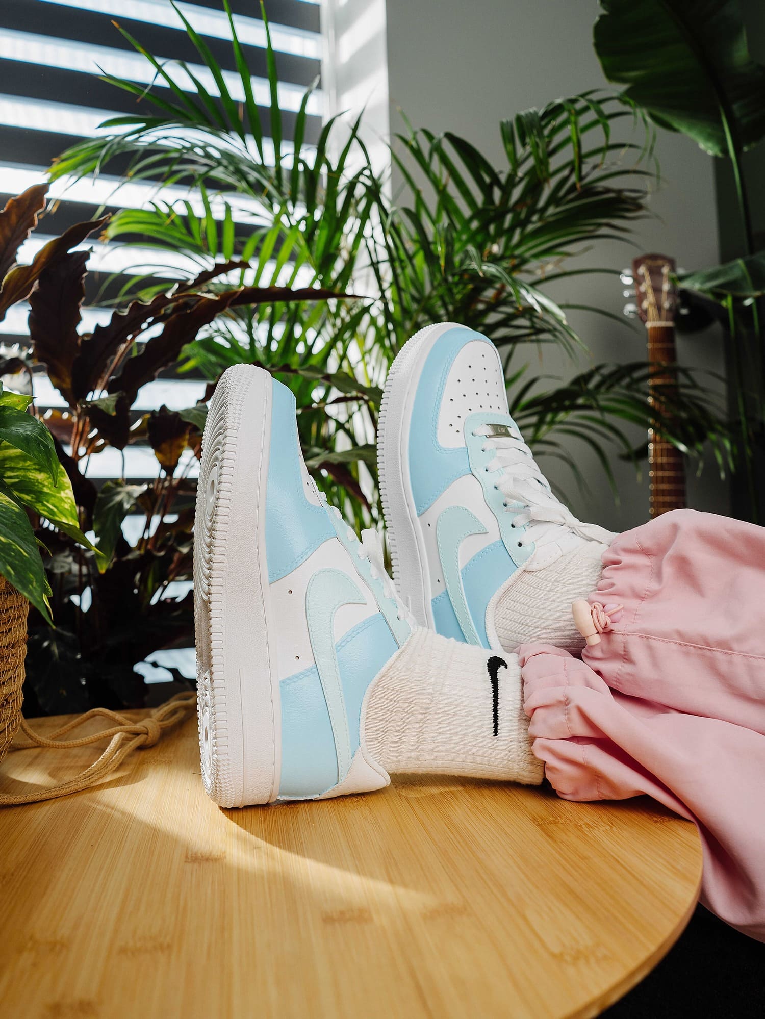 Close-up of legs wearing custom light blue Air Force 1 sneakers, styled with pink pants and Nike socks, highlighting the fresh, stylish design.