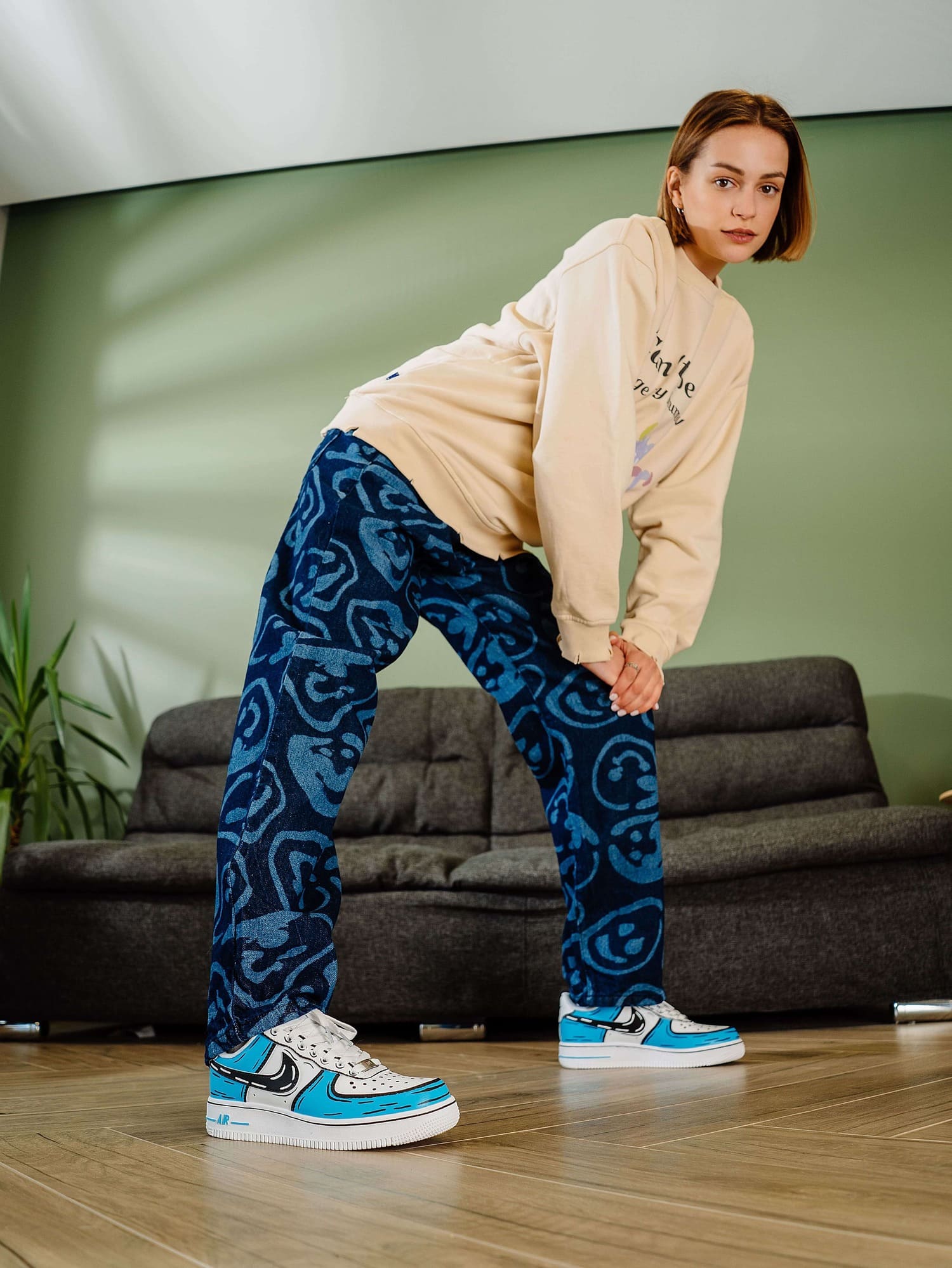 Model wearing personalized custom Air Force 1 sneakers with blue cartoon-style design, in a stylish indoor setting.